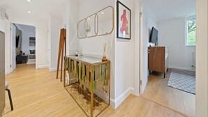 Een modern interieur met een houten vloer, een console tafel met glazen blad, een spiegel, een ingelijst kunstwerk, een televisie en een houten kast.