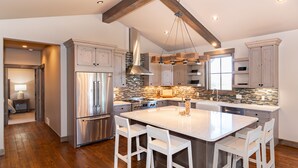 A spacious kitchen with a large island, wooden beams, stainless steel appliances, and a tiled backsplash. - Mountainside Vista - Luxury Home with Stunning Views - Ski In / Ski Out! (Granby)