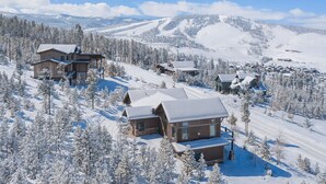 A snow-covered mountain resort with multiple wooden cabins and a ski slope. - Mountainside Vista - Luxury Home with Stunning Views - Ski In / Ski Out! (Granby)