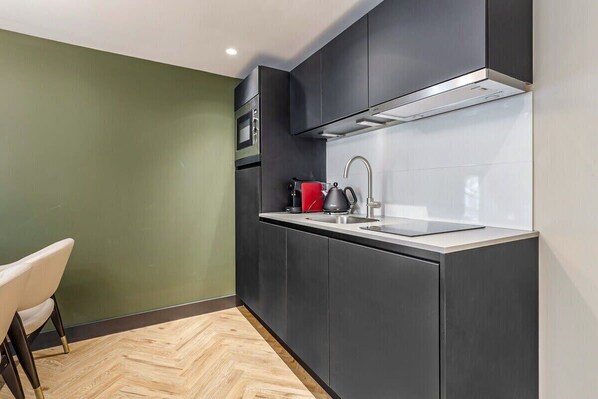 Una cucina moderna con mobili scuri, un lavello in acciaio inossidabile e un bollitore rosso.