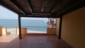 A balcony with a view of the sea, a tiled floor, and a wooden ceiling.