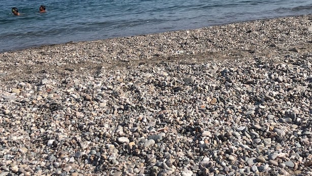 A pebbled beach with a clear sky and calm sea.