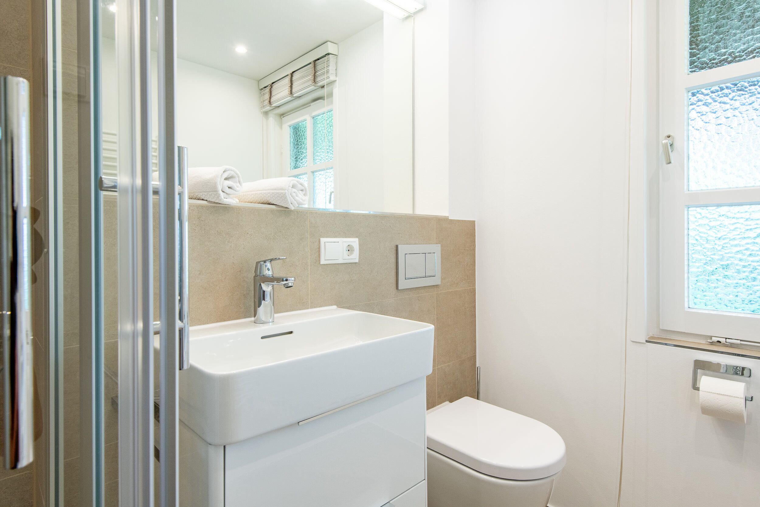 Un baño moderno con un lavamanos blanco, un inodoro y una ventana con vistas.