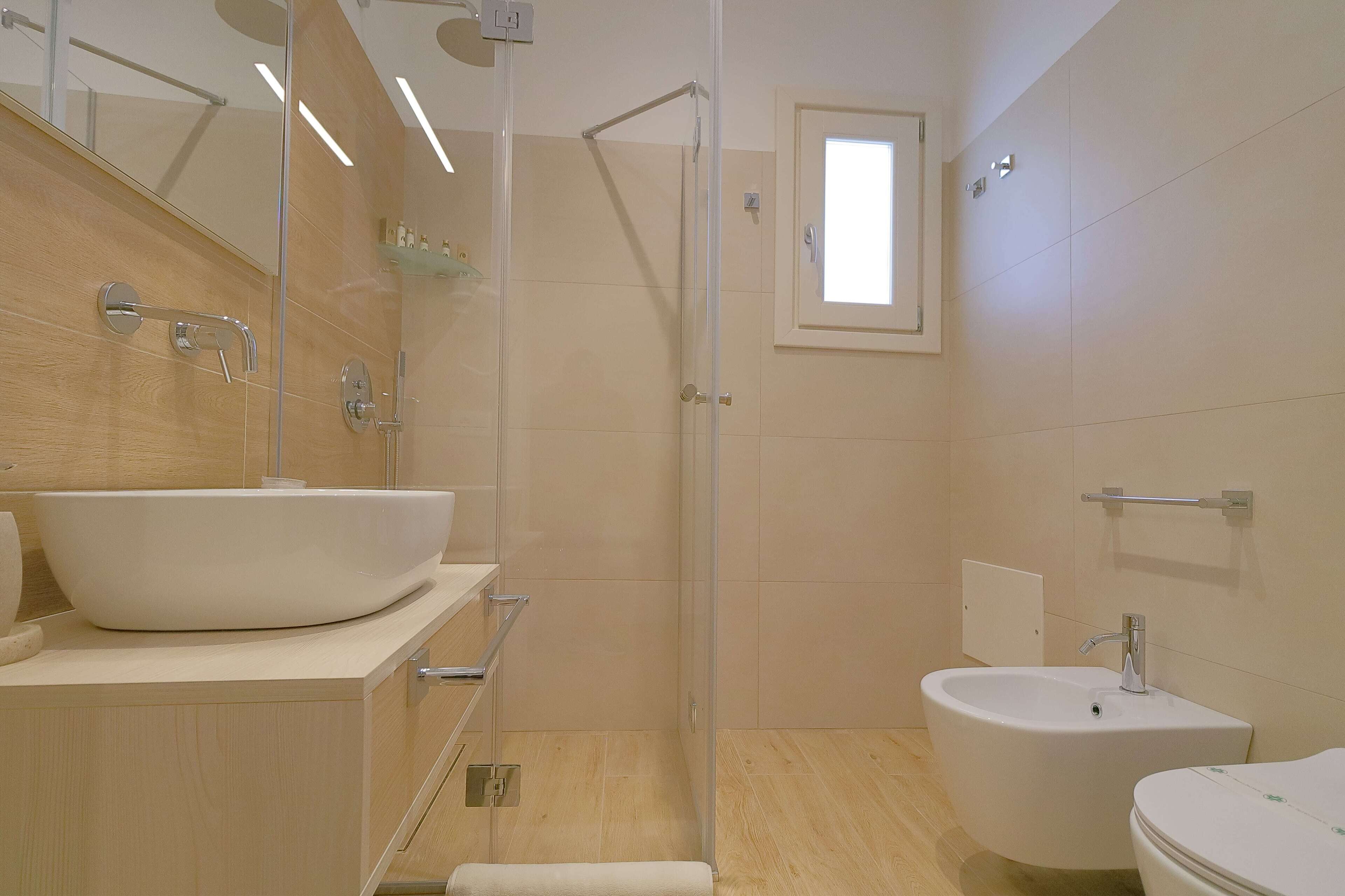 Un baño moderno con un lavamanos grande de color blanco, un lavabo aparte y una zona de ducha con mampara de cristal.
