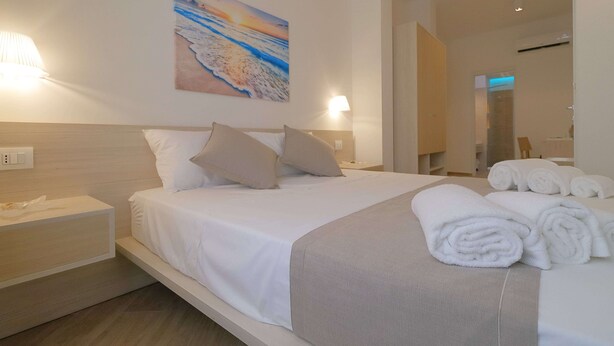 Una camera d'albergo moderna con un letto rifatto, un quadro raffigurante una spiaggia e un bagno visibile attraverso una porta aperta.