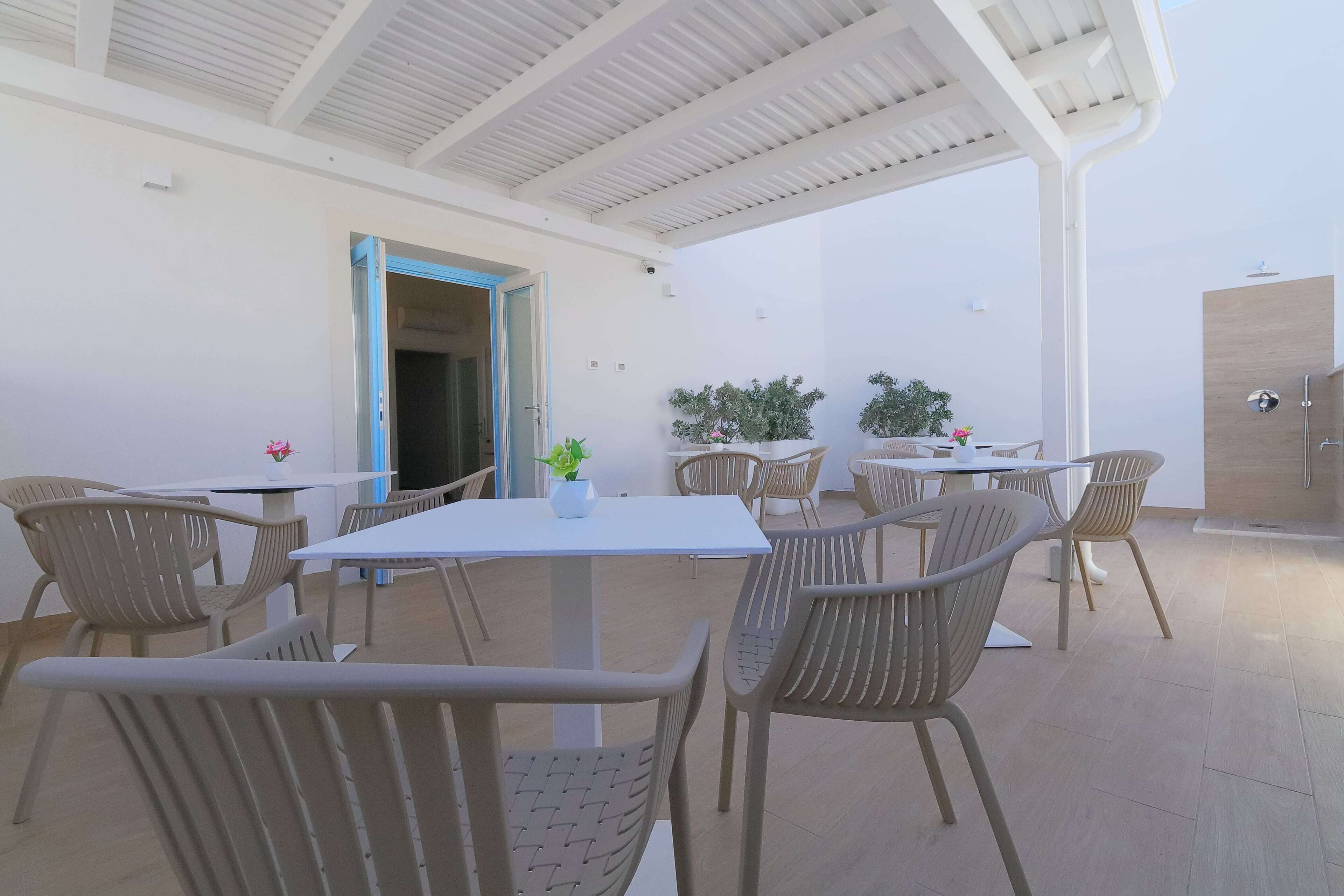 Un espace extérieur abrité, aménagé pour les repas, avec des tables et des chaises, une porte donnant sur une autre pièce et des plantes en pot.