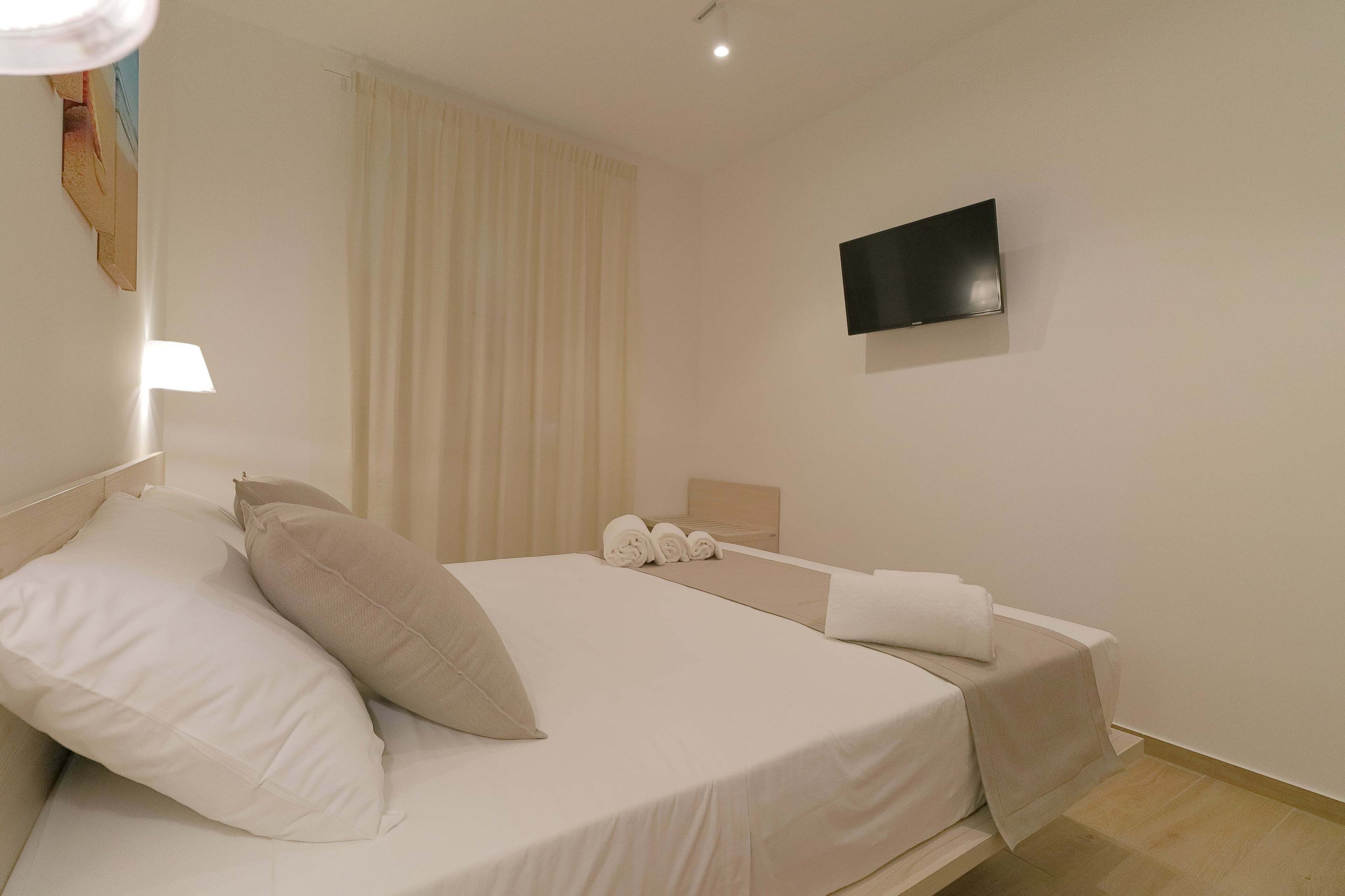 A hotel room with a bed, a TV mounted on the wall, and a window with curtains.