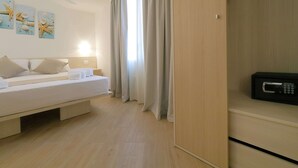 Una camera d'albergo moderna con un letto, comodini, un forno a microonde e vista sul mare attraverso ampie finestre.