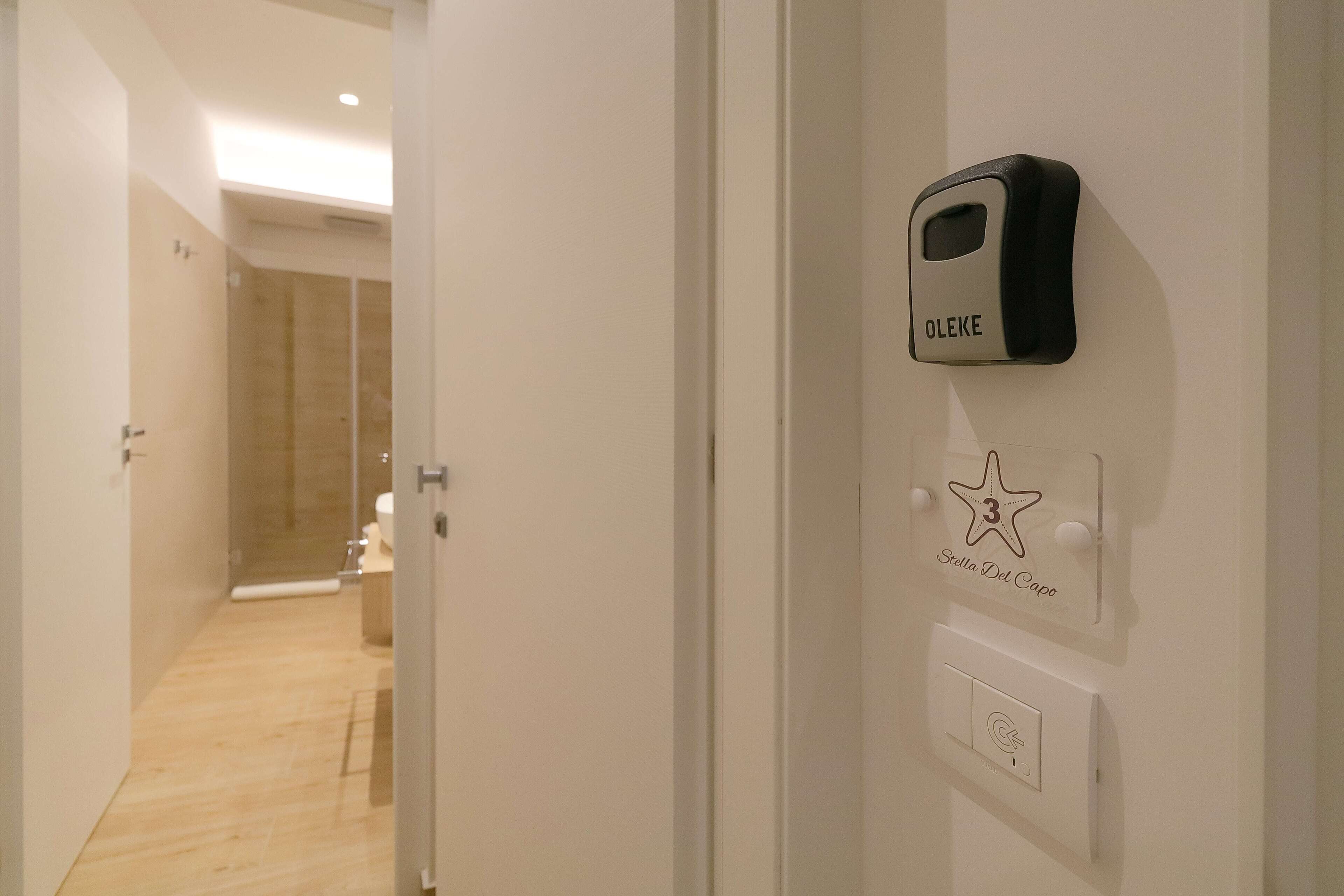 A hotel room with a shower, a toilet, and a wall-mounted control panel labeled "OLEKE".