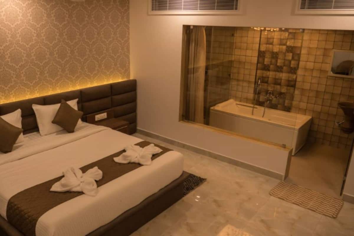 A modern hotel room with a large bed, a separate bathroom with a glass shower, and a patterned wall.
