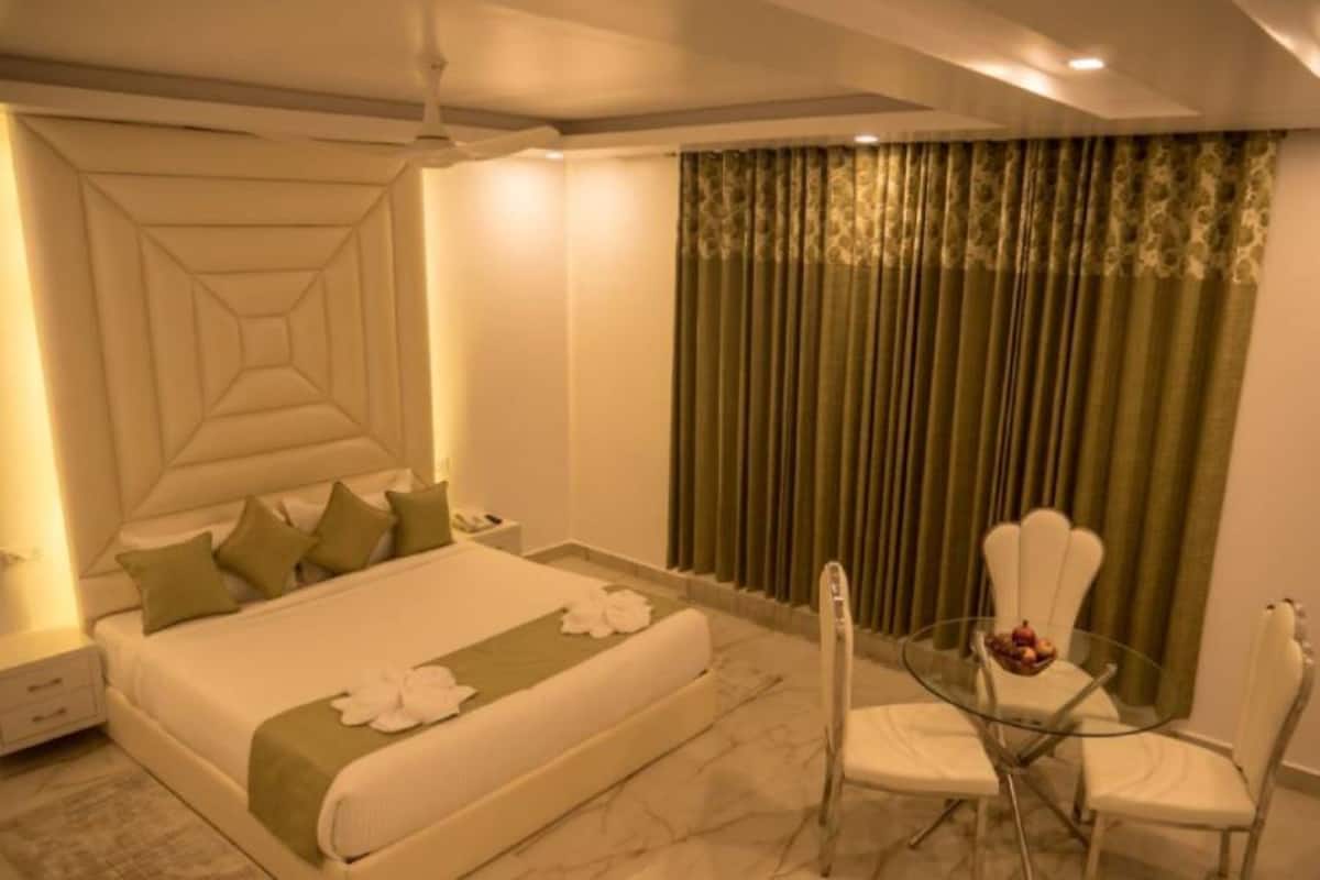 A hotel room with a large bed, a glass table with chairs, and a green curtain.