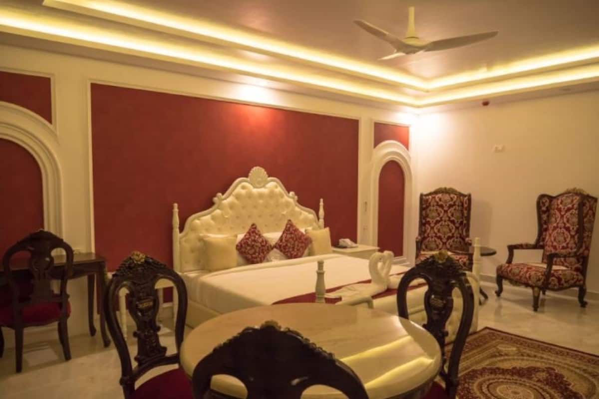A hotel room with a large bed, two chairs, a table, and a ceiling fan.
