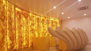 A modern interior with a marble-like wall, a unique sculptural bench, and a reception desk. - Hotel Blue Waves (Port Blair)