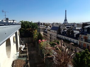A rooftop terrace with a view of the Eiffel Tower, featuring a wooden deck, potted plants, and a metal railing. - Luxury 2 Bdr Duplex Apt with A.C. & Elevator, 2 Terraces & view on EIFFEL TOWER (Paris)