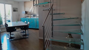 A modern interior with a glass staircase, a dining area with a table and chairs, and a kitchen with blue cabinets. - Luxury 2 Bdr Duplex Apt with A.C. & Elevator, 2 Terraces & view on EIFFEL TOWER (Paris)