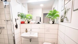 A modern bathroom with a shower, sink, toilet, and two potted plants. - Premium Studio | 1 Min to HBF (Mannheim)