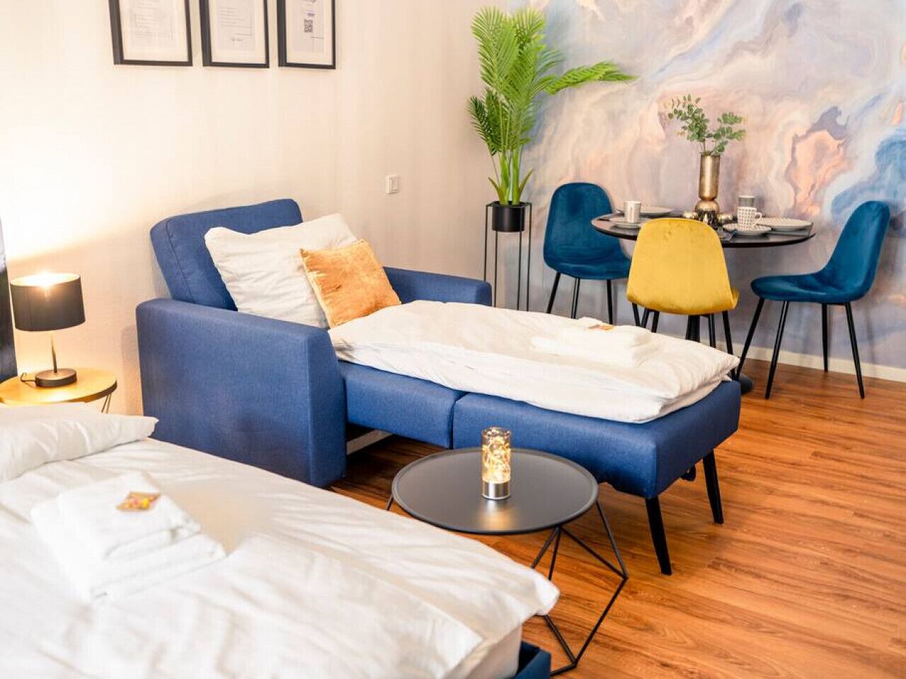 Une chambre d’hôtel moderne avec un canapé bleu, une petite table à manger avec des chaises, une plante en pot et un mur en marbre.