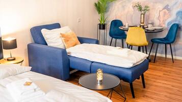 Une chambre d’hôtel moderne avec un canapé bleu, une petite table à manger avec des chaises, une plante en pot et un mur en marbre.