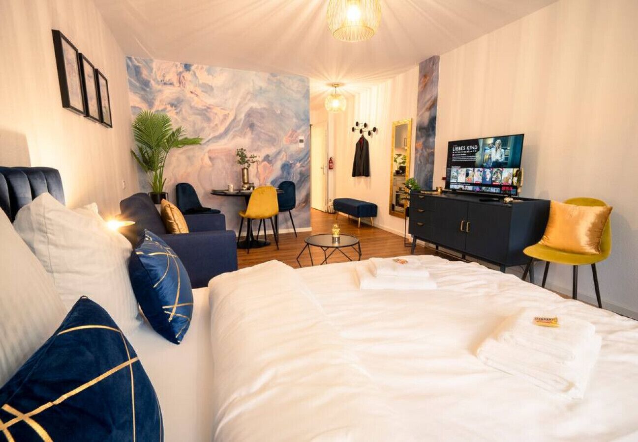A hotel room with a large bed, a desk, a TV, and a seating area with chairs.