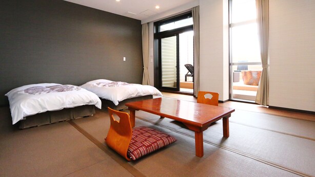 Habitación con dos camas, una mesa de madera y vistas a un espacio exterior por una puerta corredera grande.