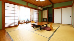 Una habitación japonesa tradicional con suelo de tatami, una mesa de madera baja, puertas correderas y un ventilador de techo.