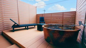Una terraza de madera con un jacuzzi, una silla de descanso y una mesita.