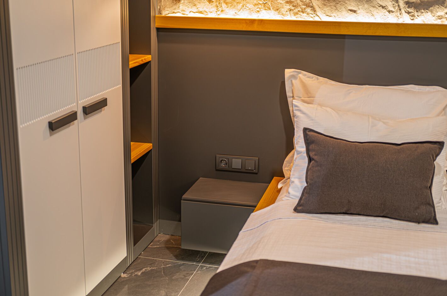 Une chambre à coucher comprenant un lit, une table de chevet, une étagère fixée au mur et un panneau de commande.