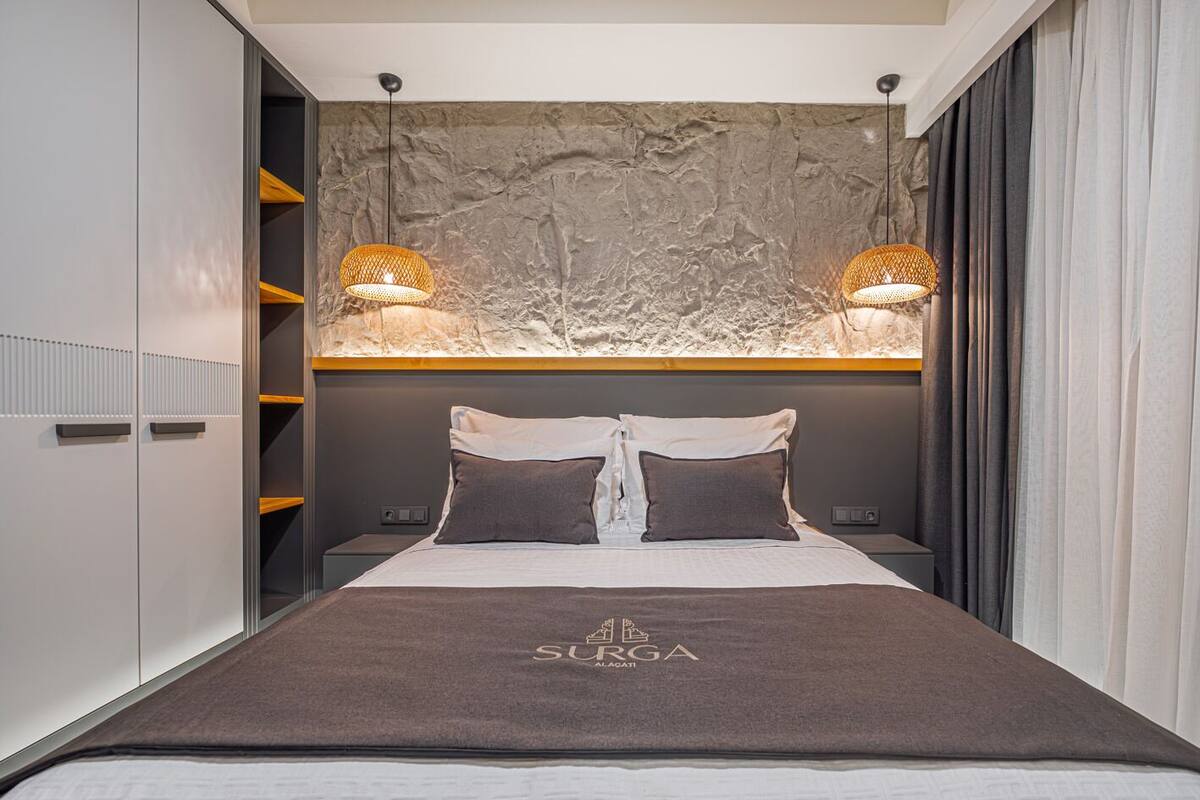 Un dormitorio moderno con cama, dos lámparas de noche, un armario y una pared texturizada detrás de la cama.