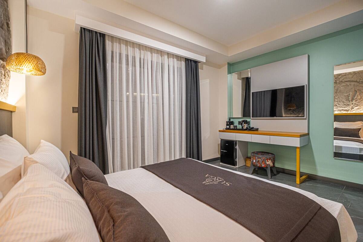 Una habitación de hotel con cama, escritorio, espejo y ventana con cortinas.