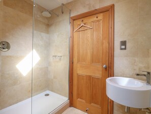 A bathroom with a wooden door, a glass shower enclosure, a white sink, and beige tiled walls. - Old Print House (Ilkeston)