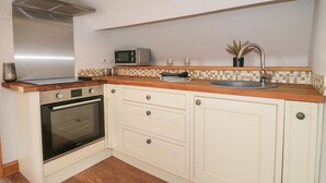 A compact kitchen with a microwave, oven, and stainless steel range hood. - Old Print House (Ilkeston)
