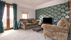 A living room with a sofa, ottoman, and a television on a stand. - Old Print House (Ilkeston)