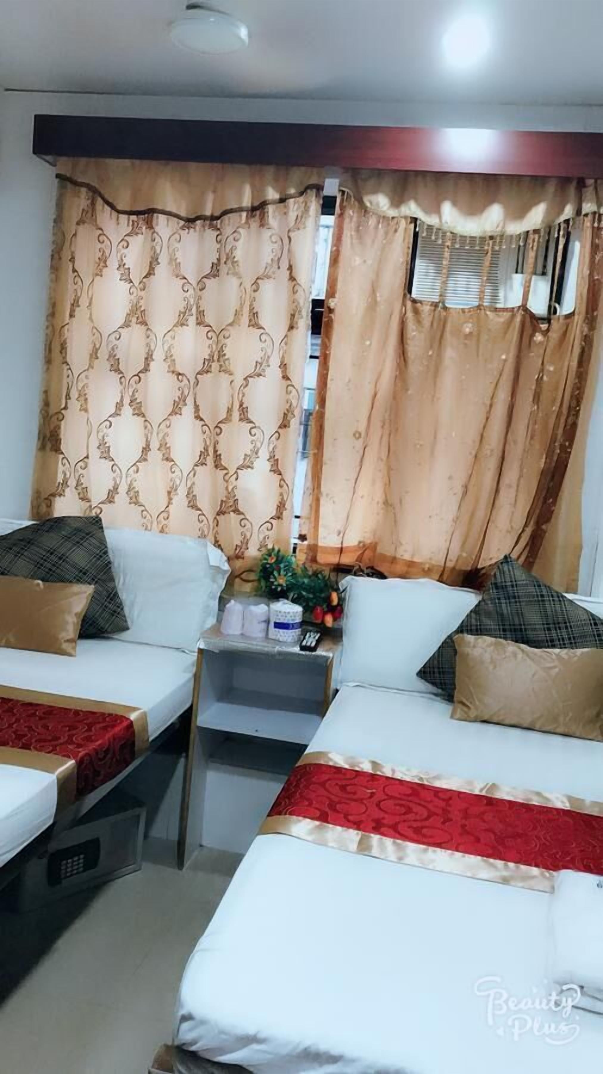 A hotel room with two beds, each with a red and white bedspread, and a small table with a plant and toiletries.