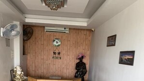 A reception area with a wooden reception desk, a grey sofa, and a fan. - Airport Hotel (Port Blair)