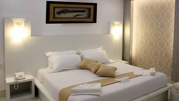 A hotel room with a large bed, white bedding, a bedside phone, and a framed picture on the wall. - Airport Hotel (Port Blair)