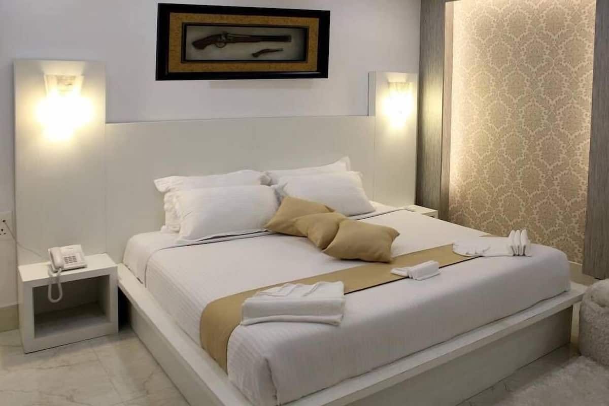 A hotel room with a large bed, white bedding, a bedside phone, and a framed picture on the wall.