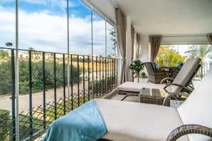 A balcony with wicker furniture, a view of greenery, and a clear sky.