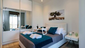 Une chambre d’hôtel moderne avec un grand lit, une table de chevet, une commode, un miroir et un tableau au mur.