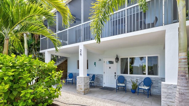 A modern building with a balcony, numbered 26, and a covered entrance with chairs and a potted plant. - Pennekamp Hideaway | Water View, Kayaks & Pool Table (Key Largo)