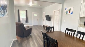 A spacious dining area with a wooden table and chairs, a sofa, and a television mounted on the wall. - 3rd Base Apt 1 - All Star Baseball Rentals (Oneonta)
