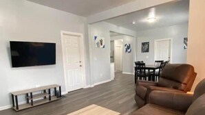 A modern living room with a brown leather sofa, a wooden coffee table, and a flat-screen TV mounted on the wall. - 3rd Base Apt 1 - All Star Baseball Rentals (Oneonta)