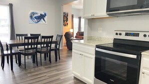 A modern kitchen with a built-in oven and microwave, a dining area with a table and chairs, and a living area with a couch and a coffee table. - 3rd Base Apt 1 - All Star Baseball Rentals (Oneonta)