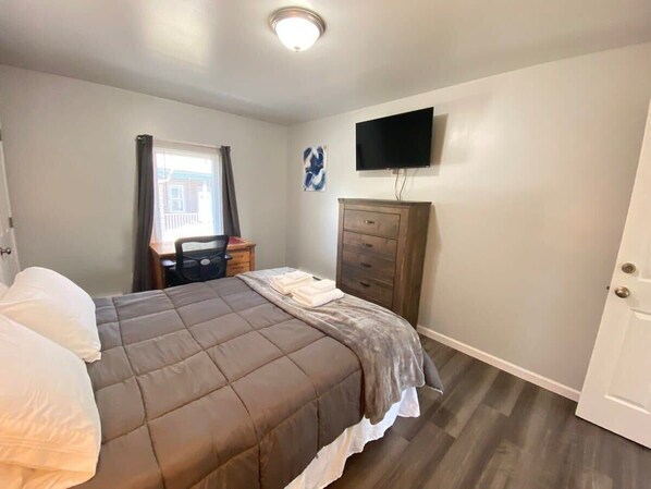 Quarto com cama, penteadeira, televisão e janela com cortinas.