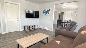 A modern living room with a wooden coffee table, a brown leather sofa, and a flat-screen TV mounted on the wall.