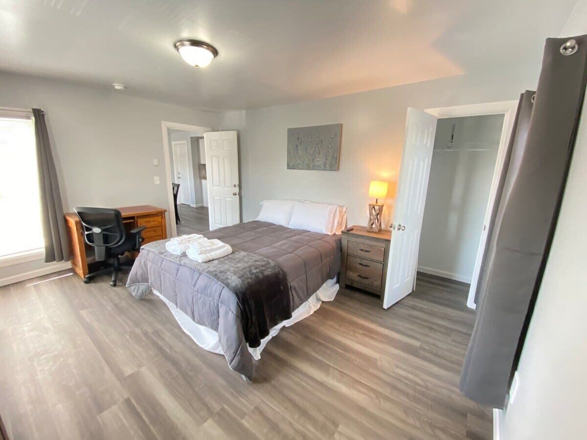 A bedroom with a bed, a desk, a chair, a nightstand, and a lamp.