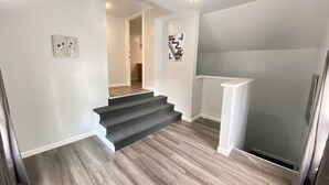 A staircase with a wooden finish, a white wall with a picture, and a light fixture on the ceiling. - Double Play Apt 1 - All Star Baseball Rentals (Oneonta)