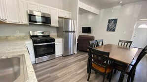 A modern kitchen with white cabinets, stainless steel appliances, and a wooden dining table with chairs. - Double Play Apt 1 - All Star Baseball Rentals (Oneonta)