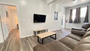 A modern living room with a brown leather sofa, a wooden coffee table, and a flat-screen TV mounted on the wall. - Double Play Apt 1 - All Star Baseball Rentals (Oneonta)