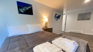 A hotel room with a large bed, a bedside table with a lamp, and artwork on the walls. - Double Play Apt 1 - All Star Baseball Rentals (Oneonta)