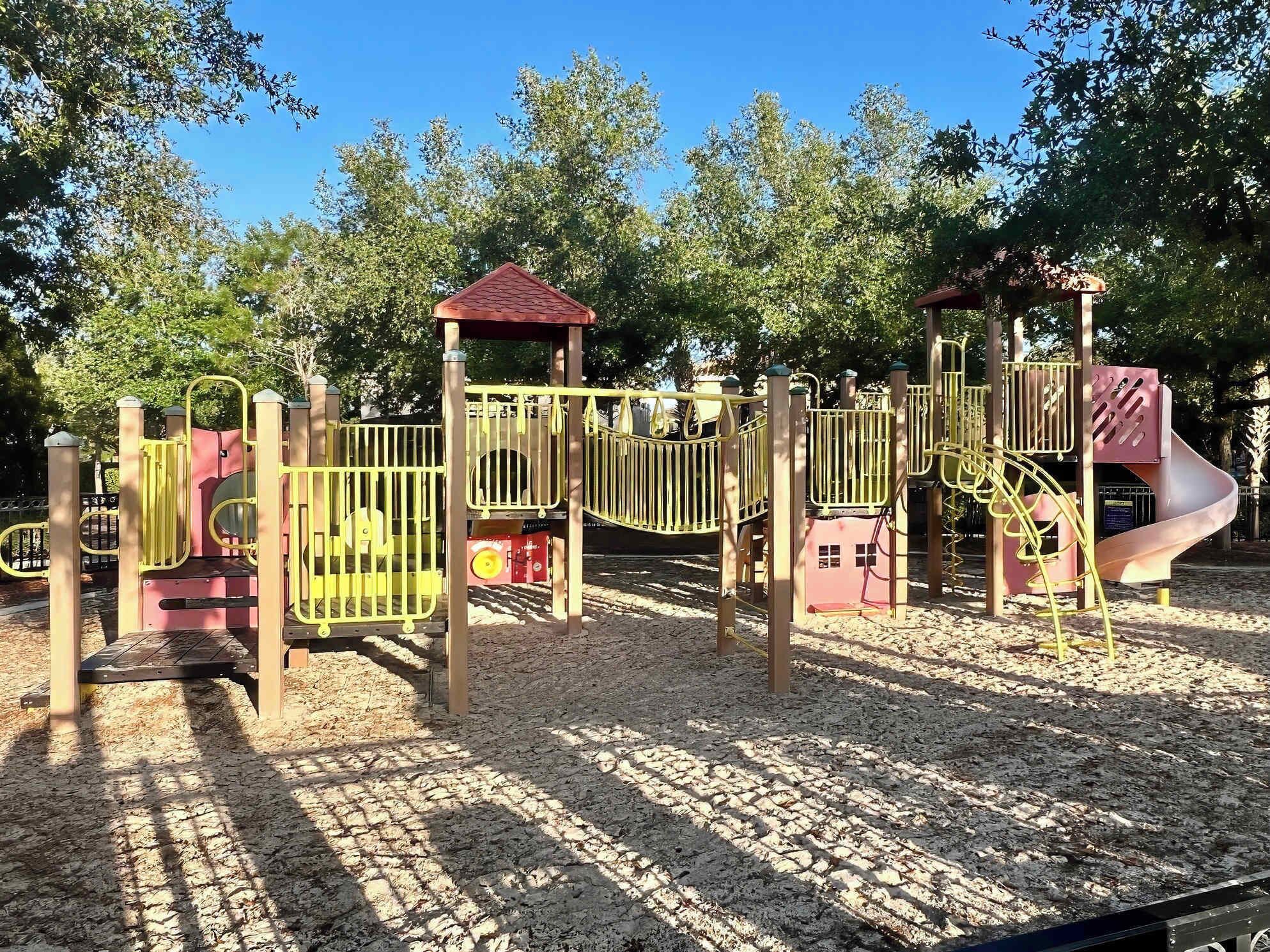A playground with various play structures including a slide, climbing areas, and a small building.